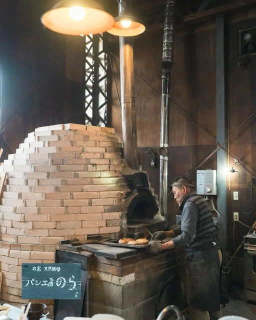 暖かな照明とレンガの薪窯に囲まれ、パンを焼く職人